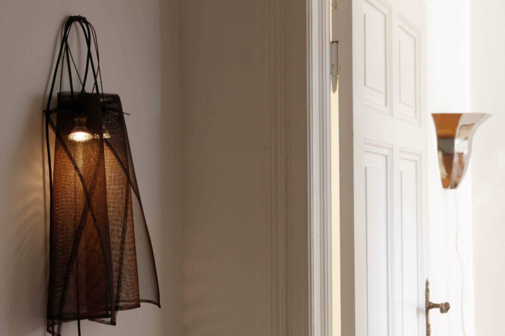 A mesh wall lamp beside a doorway, with a chrome wall light in the next room